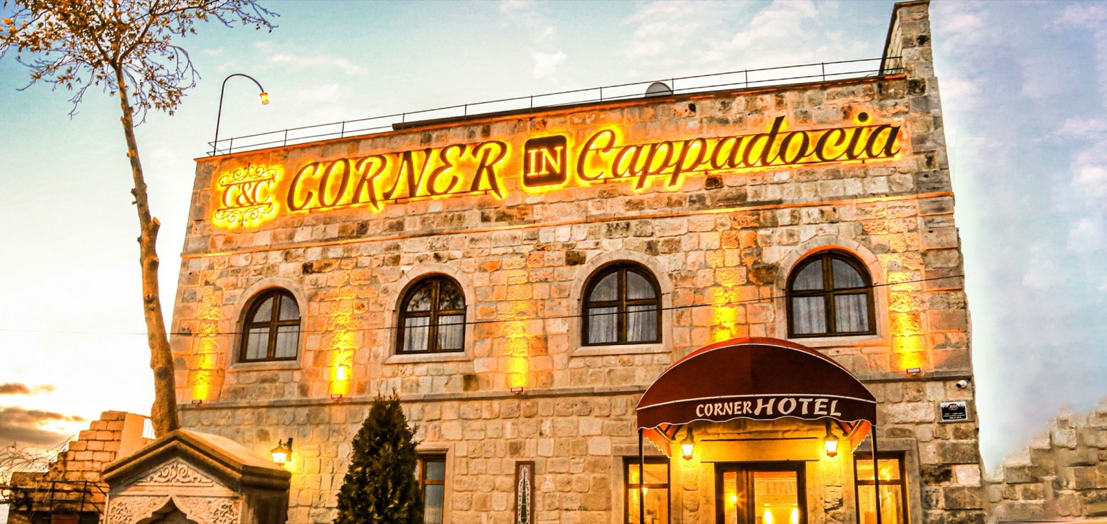 Akşam ışığında Corner in Cappadocia'nın taş cephesi ve CornerHotel tenteli girişi
