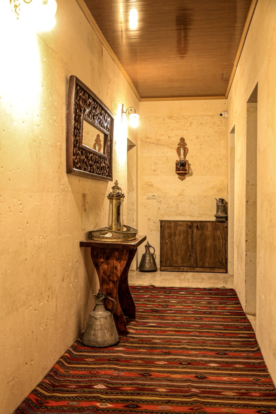 Kilim serili taş koridor, ahşap konsol ve bakır ibrikler