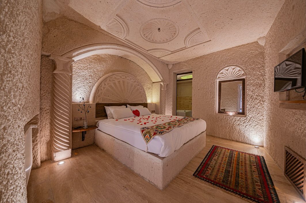 301 Deluxe Cave Room: oyma kemerli yatak nişi, tavanda taş rozetler ve kilim